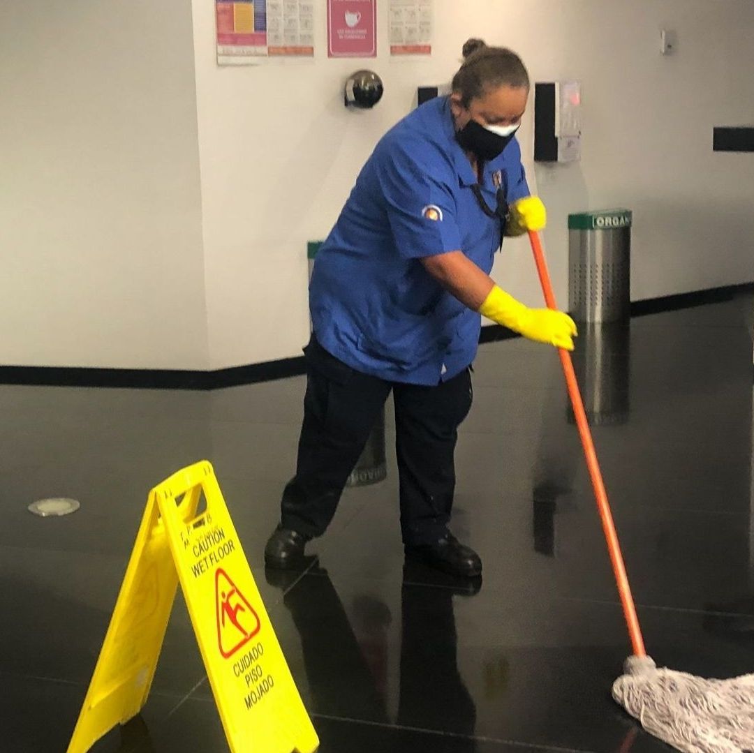 Una señora limpiando un piso con un trapeador.