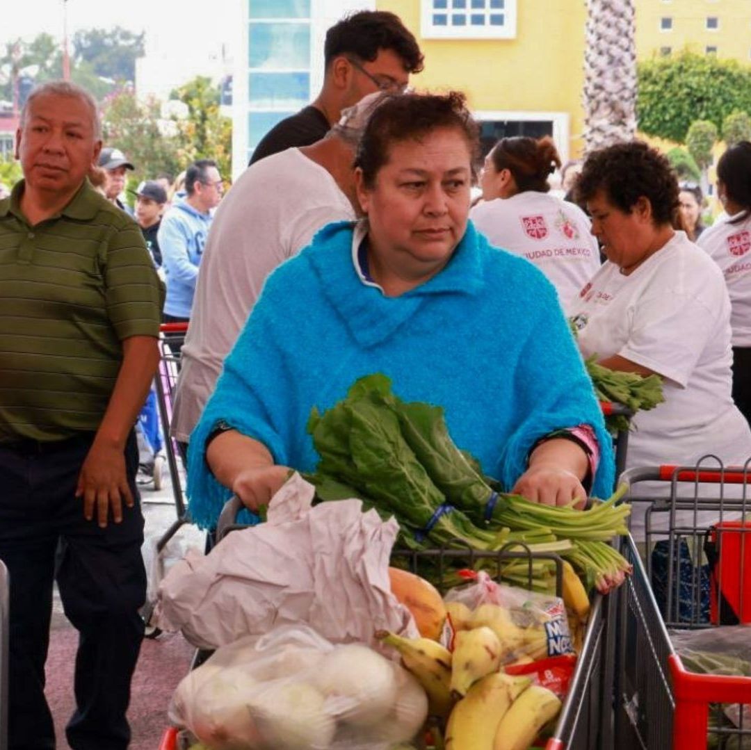 Una mujer con un carrito de comprar lleva verduras.