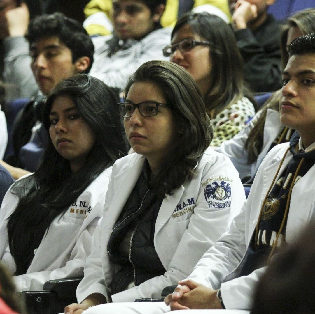 Varios estudiantes usando bata están sentados.