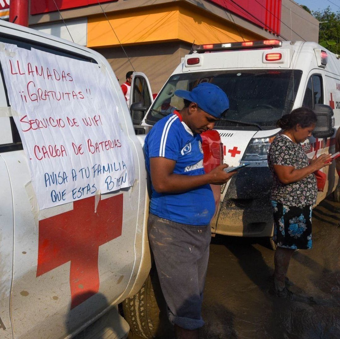Personas frente a ambulancias cargan sus celulares.
