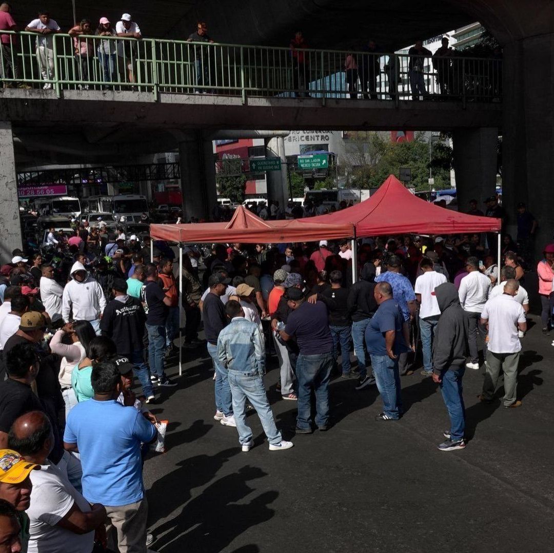 Varias personas bloquean el paso en una carretera, hay una carpa roja.