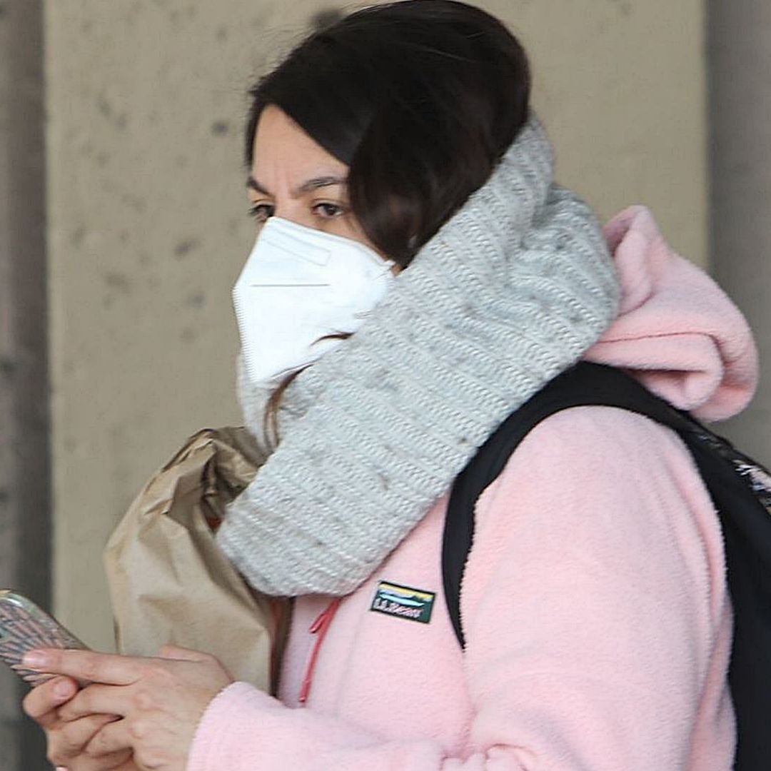 Una mujer se cubre del frío con una sudadera rosa, cubrebocas y bufanda color gris