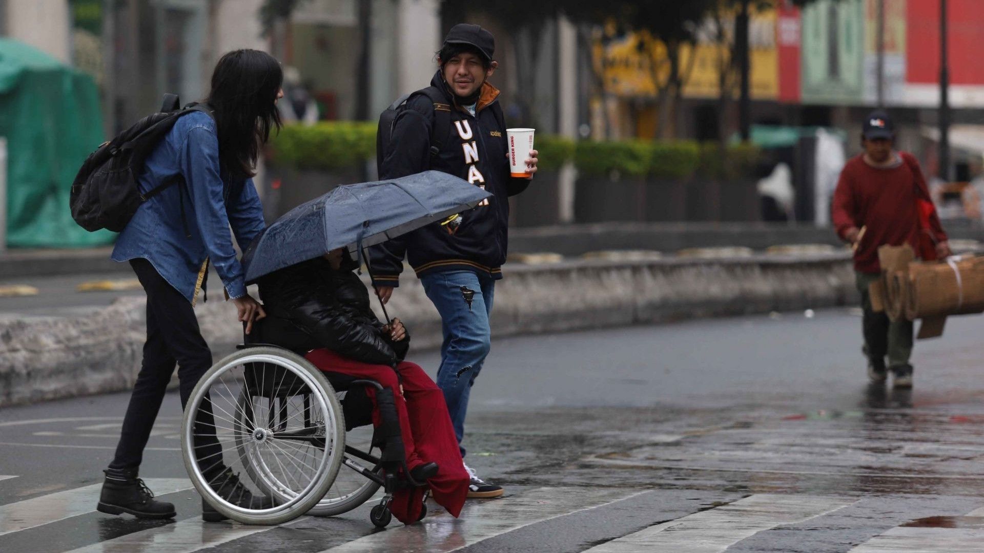 Persona en silla de ruedas es ayudada por otra persona para cruzar la calle.