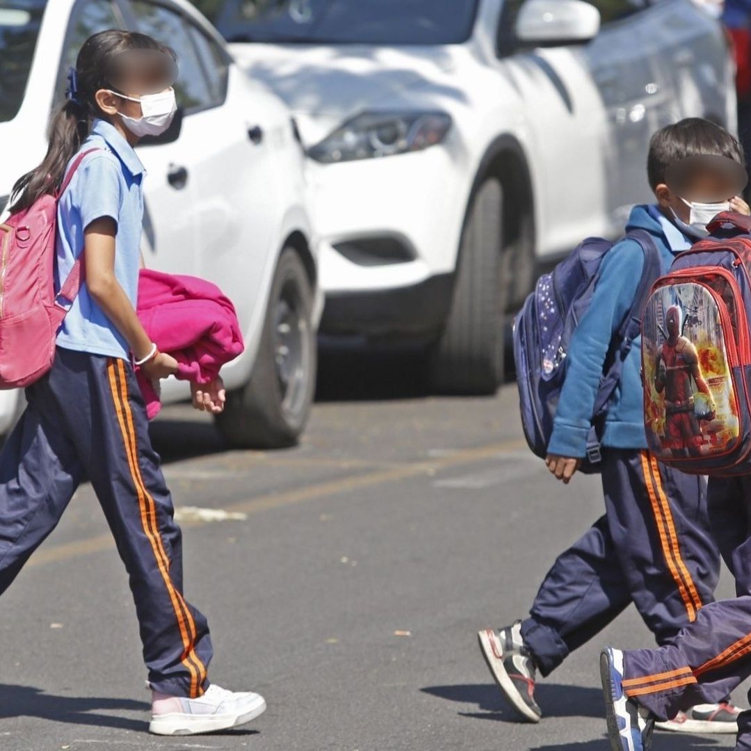 Niños con cubrebocas cruzan la calle.
