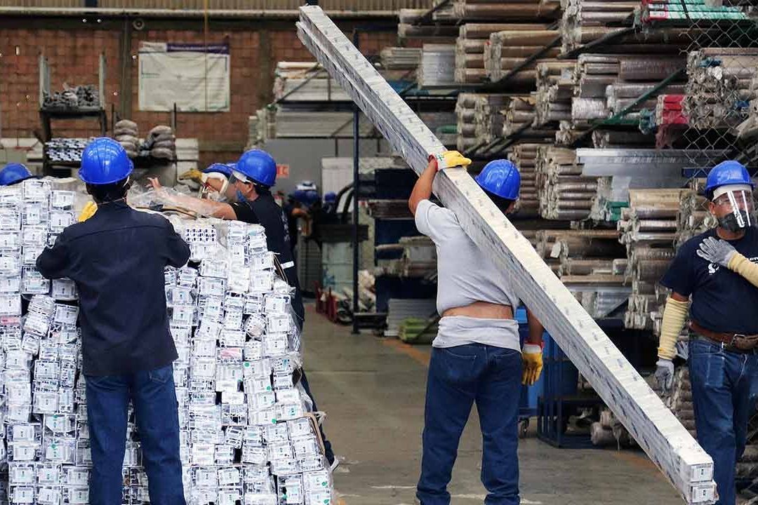 Grupo de trabajadores con cascos azules manejando materiales en un almacén industrial.