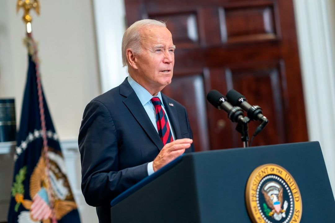 El presidente Joe Biden hablando desde un podio con el sello presidencial de Estados Unidos en una sala oficial, con banderas estadounidenses al fondo.