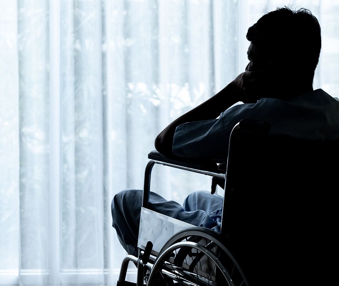 Silueta de una persona en silla de ruedas mirando por la ventana