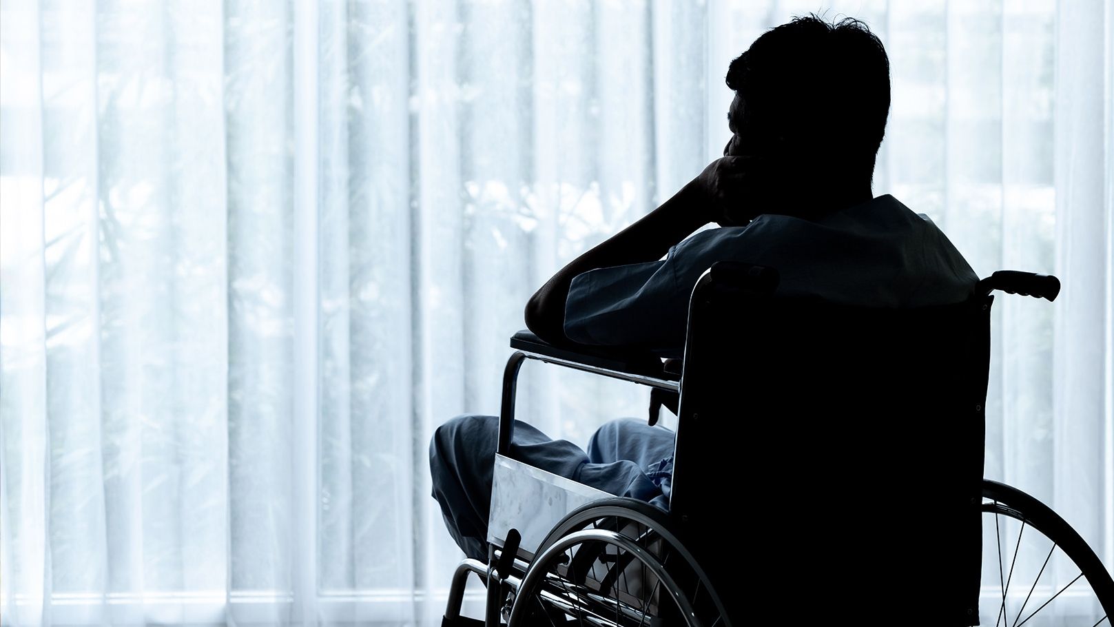Silueta de una persona en silla de ruedas mirando por la ventana