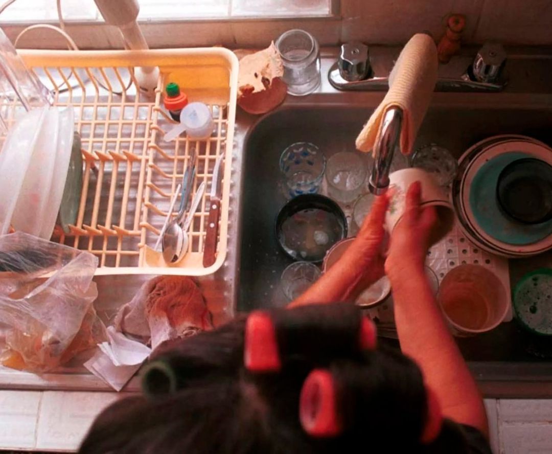 Mujer lavando platos en cocina casera.
