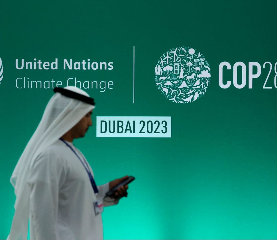 Imagen de una persona en traje tradicional árabe frente a un banner del evento COP28 de la ONU en Dubai, 2023