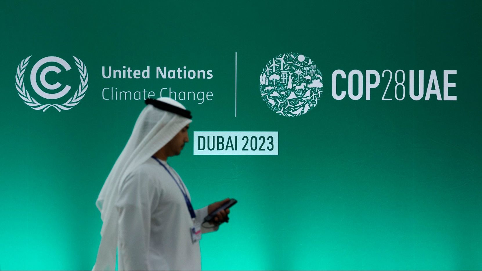 Imagen de una persona en traje tradicional árabe frente a un banner del evento COP28 de la ONU en Dubai, 2023