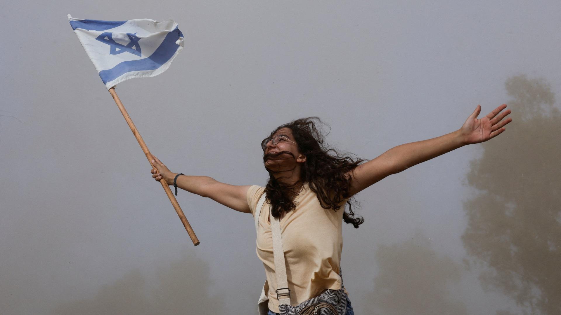 Una persona sostiene una bandera de Israel luego de que un helicóptero partió con rehenes liberados en Gaza