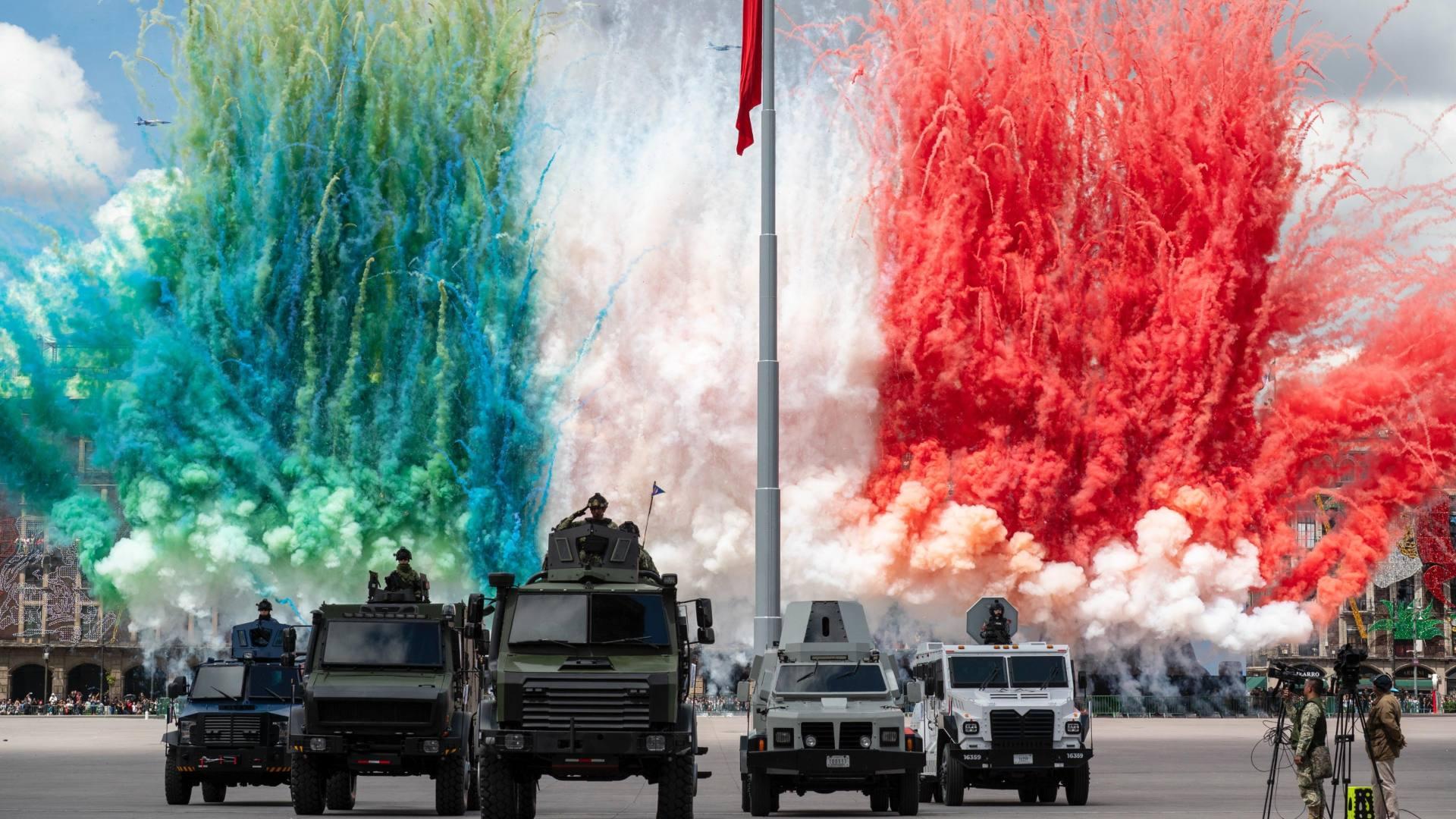 Vehículos militares con humo de colores de fondo durante desfile militar
