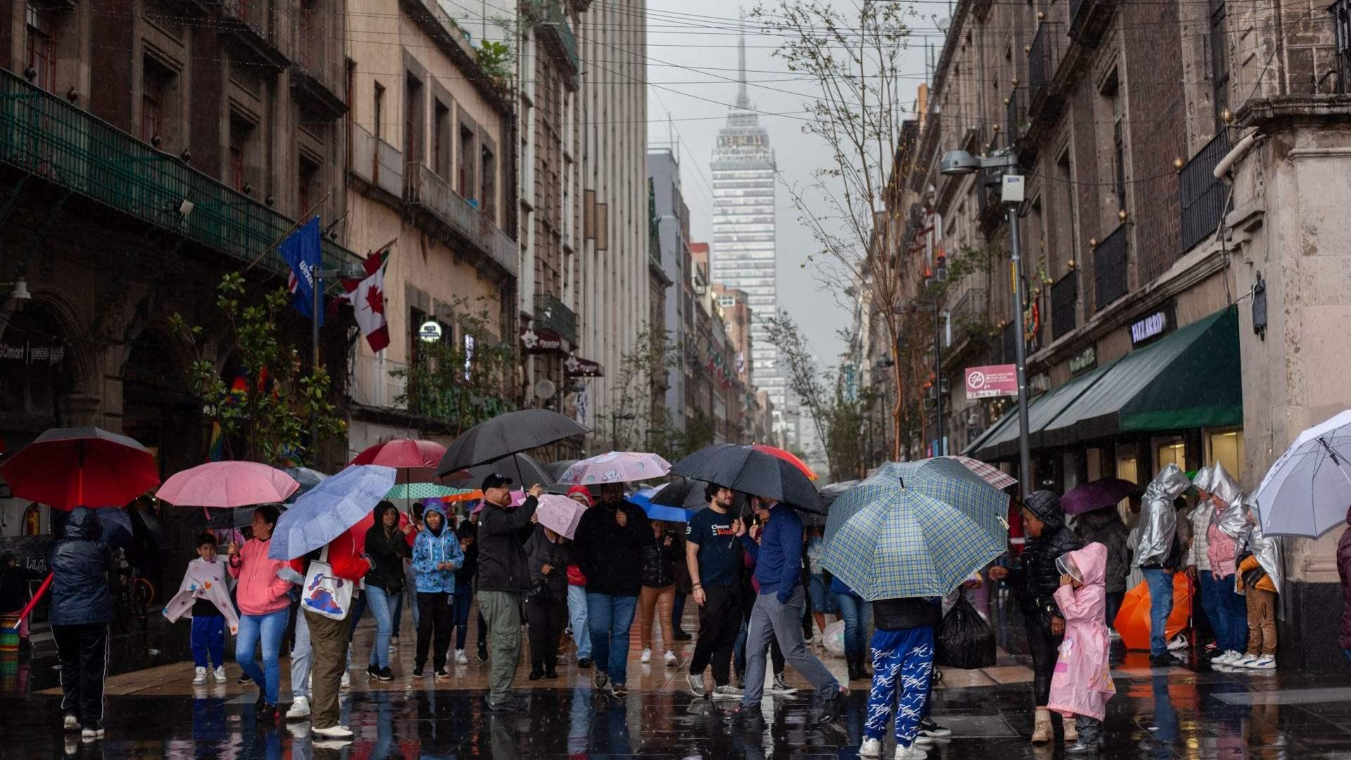 Personas con paraguas e impermeables caminan por la calle Madero