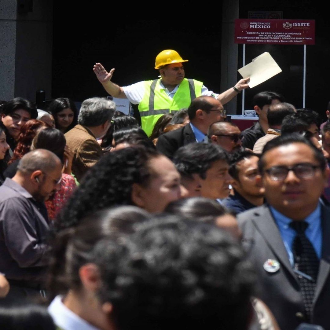 Personas salen de un edificio tras activarse la Alerta Sísmica en la Ciudad de México. Hay un elemento de Protección Civil dando instrucciones.