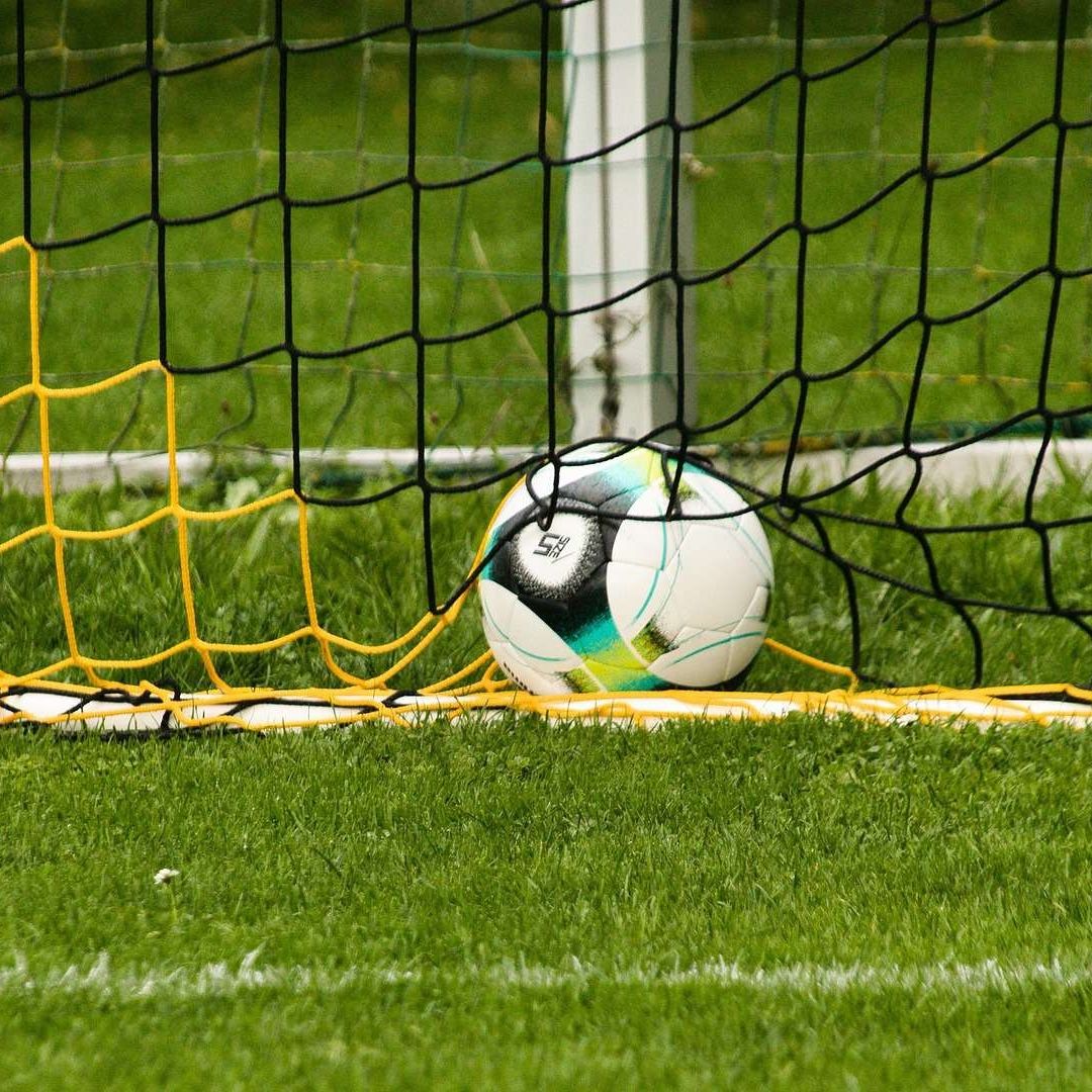 Portería en cancha de futbol con balón en la red