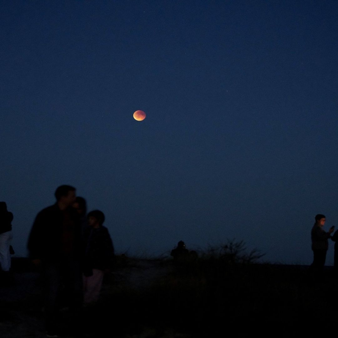Varias personas en una zona alejada de la ciudad observan la Luna brillante.