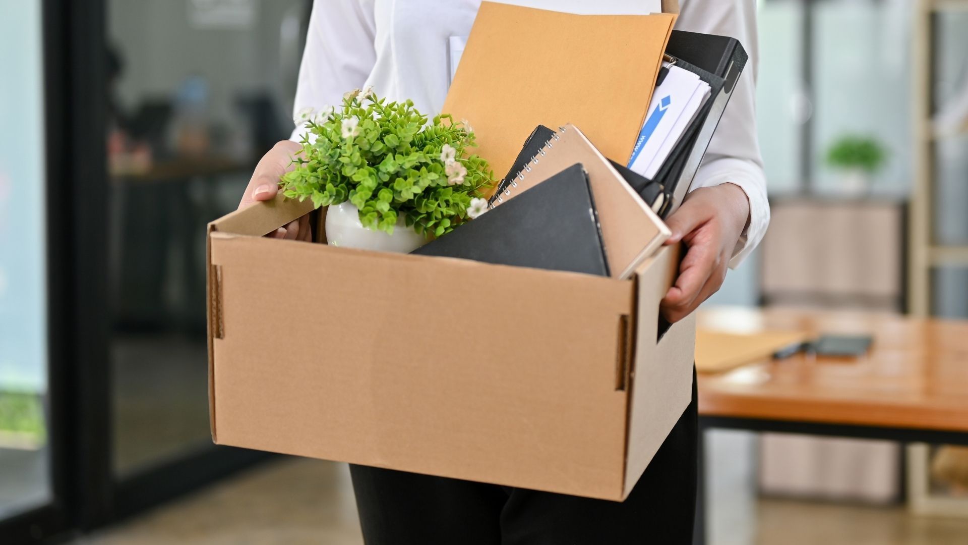 A female office worker with a cardboard box with her stuff and her resignation letter