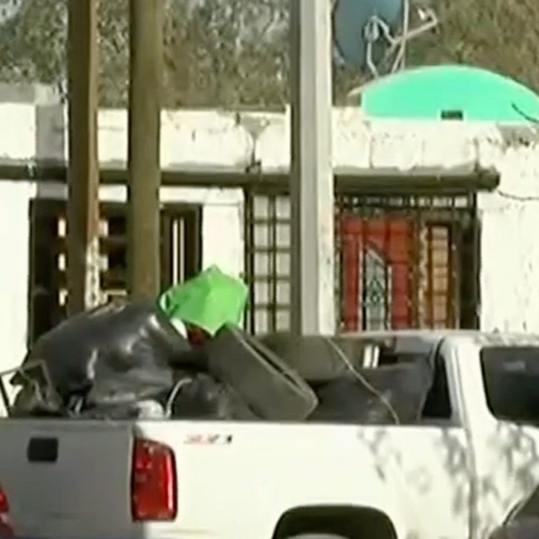 Camioneta pickup blanca cargada con bolsas negras, llantas y otros objetos
