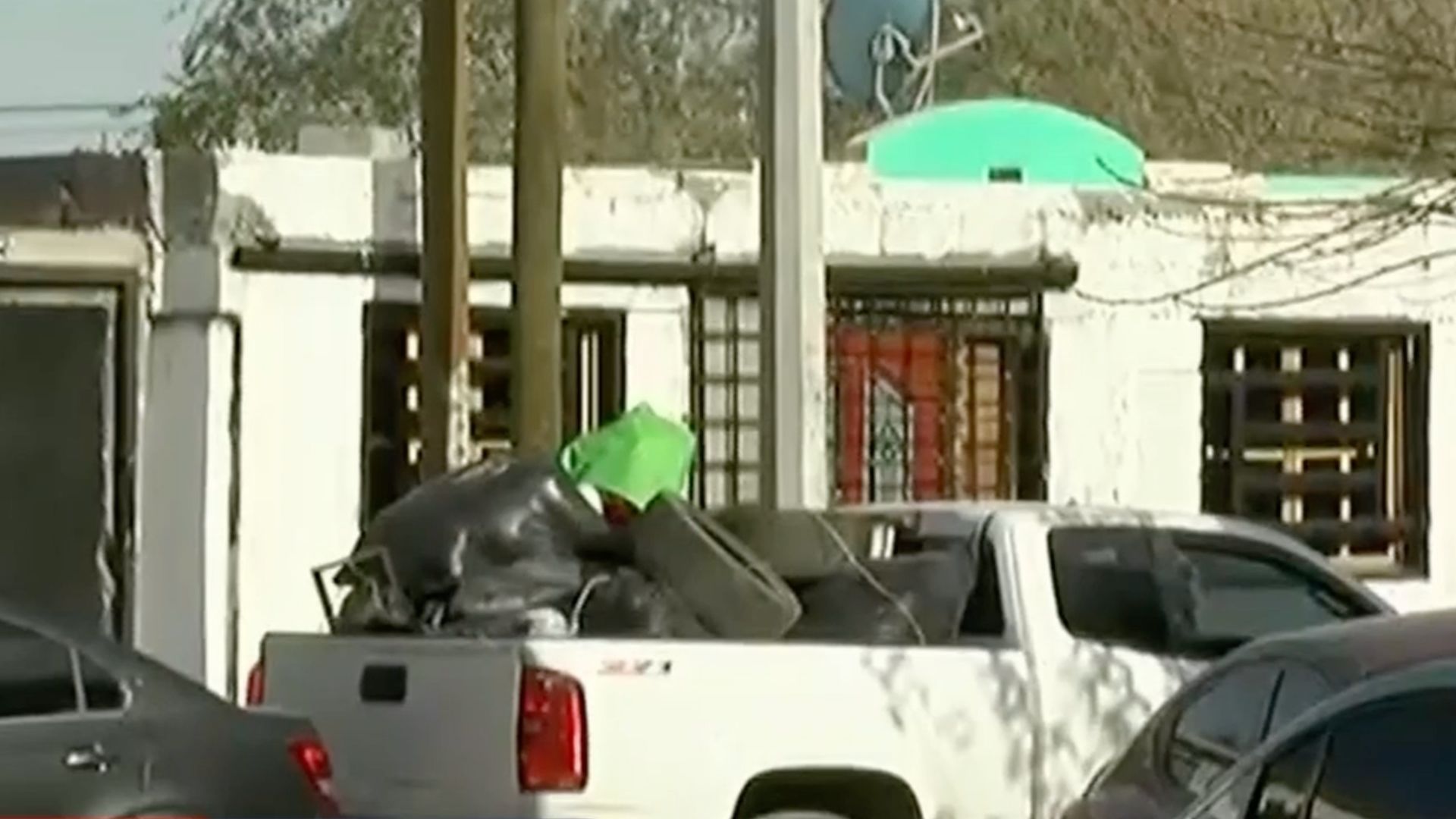 Camioneta pickup blanca cargada con bolsas negras, llantas y otros objetos