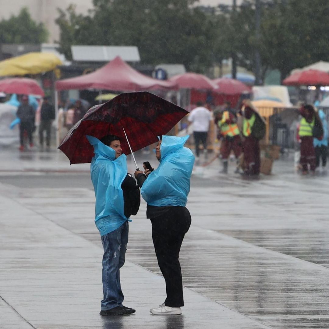 Dos personas se protegen de la lluvia con impermeables azules y un paraguas rojo