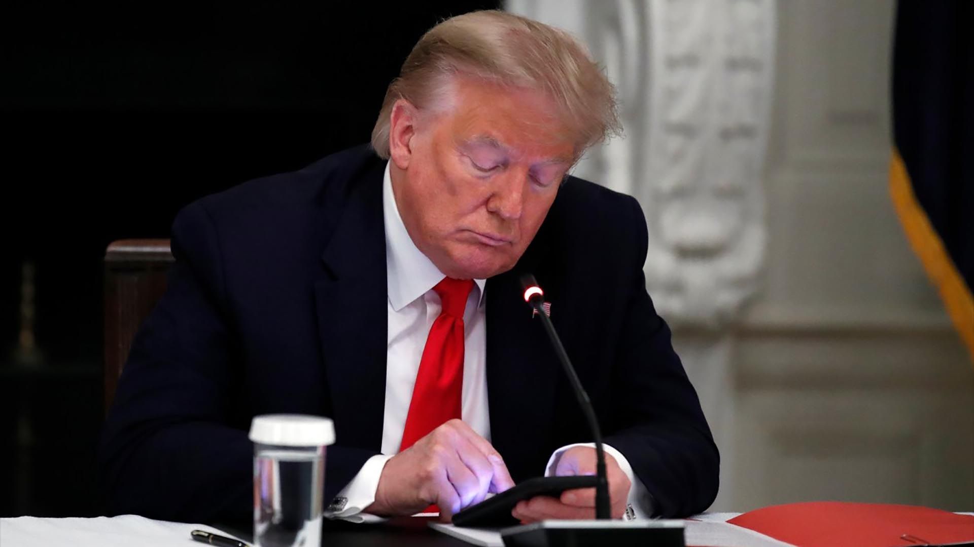 Donald Trump revisa su teléfono durante una pausa en una reunión de trabajo