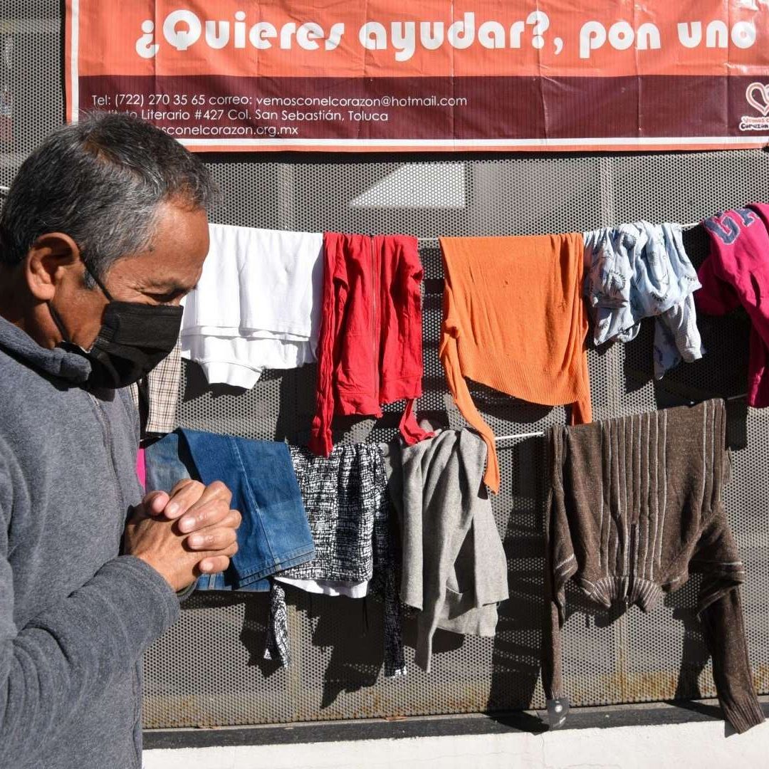 Persona camina con cubrebocas frente a tendido de ropa