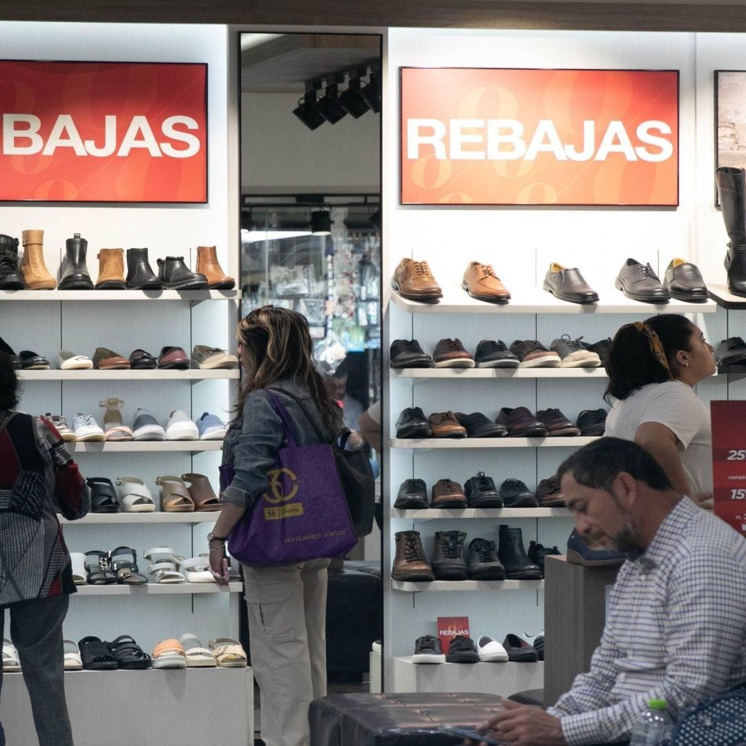 Cinco personas dentro de una zapatería observan el calzado; hay carteles que dicen "rebajas"
