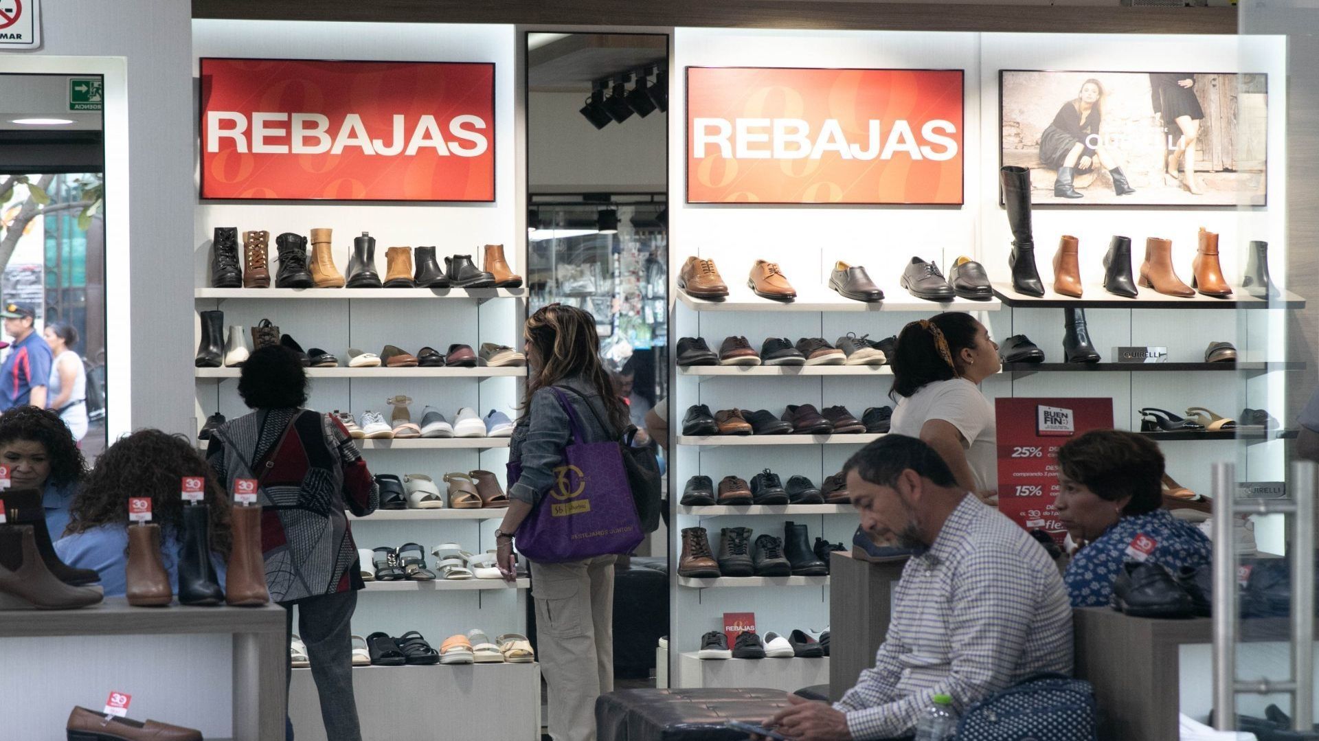 Cinco personas dentro de una zapatería observan el calzado; hay carteles que dicen "rebajas"
