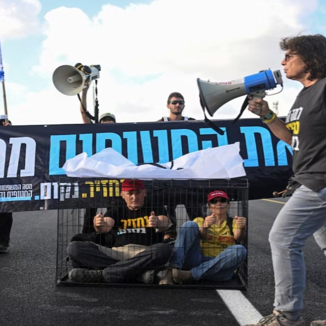 Una mujer usa un megáfono en una protesta. Detrás de ella hay dos personas en jaulas.