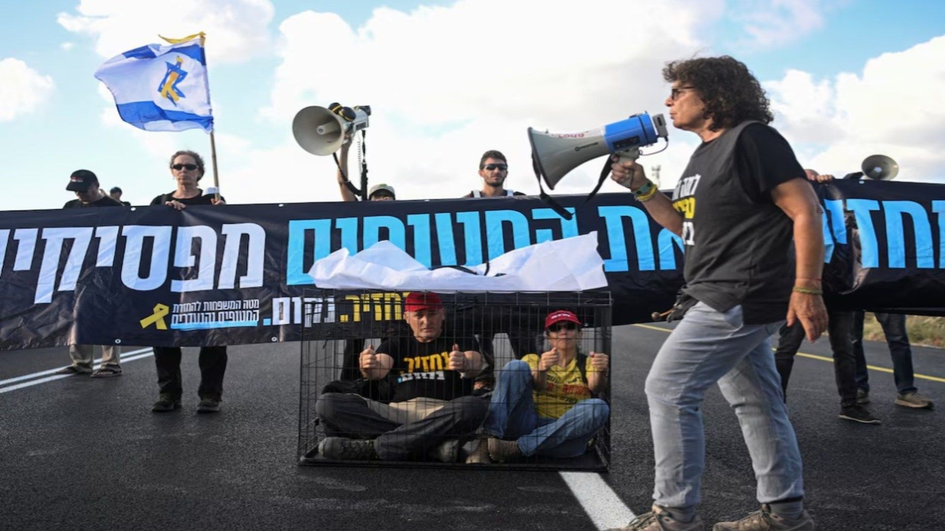 Una mujer usa un megáfono en una protesta. Detrás de ella hay dos personas en jaulas.