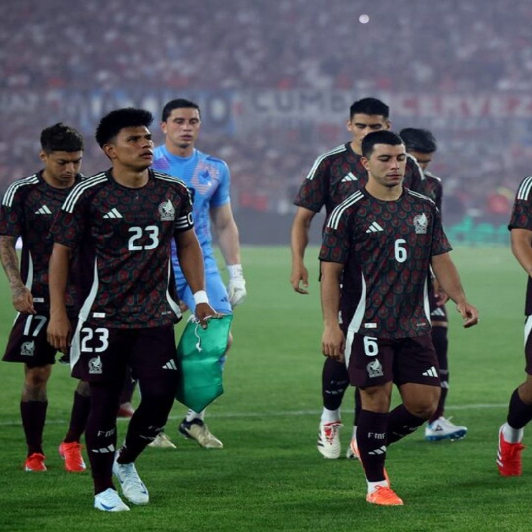 Jugadores de futbol con uniforme de color vino con negro. Tienen un semblante serio mientras caminan por las canchas.