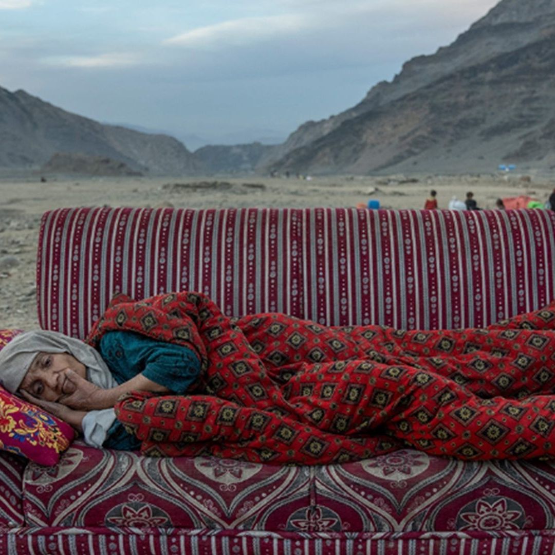 Una mujer afgana descansa en el desierto cerca de un campamento que alberga a personas recientemente deportadas de Pakistán, en Torkham, Afganistán