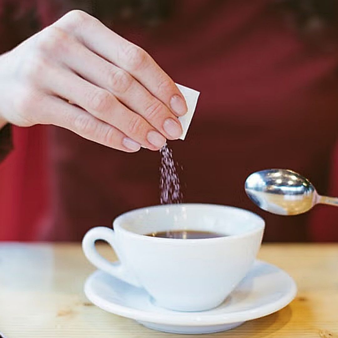 Mujer agrega sobre de edulcorante a una taza de café