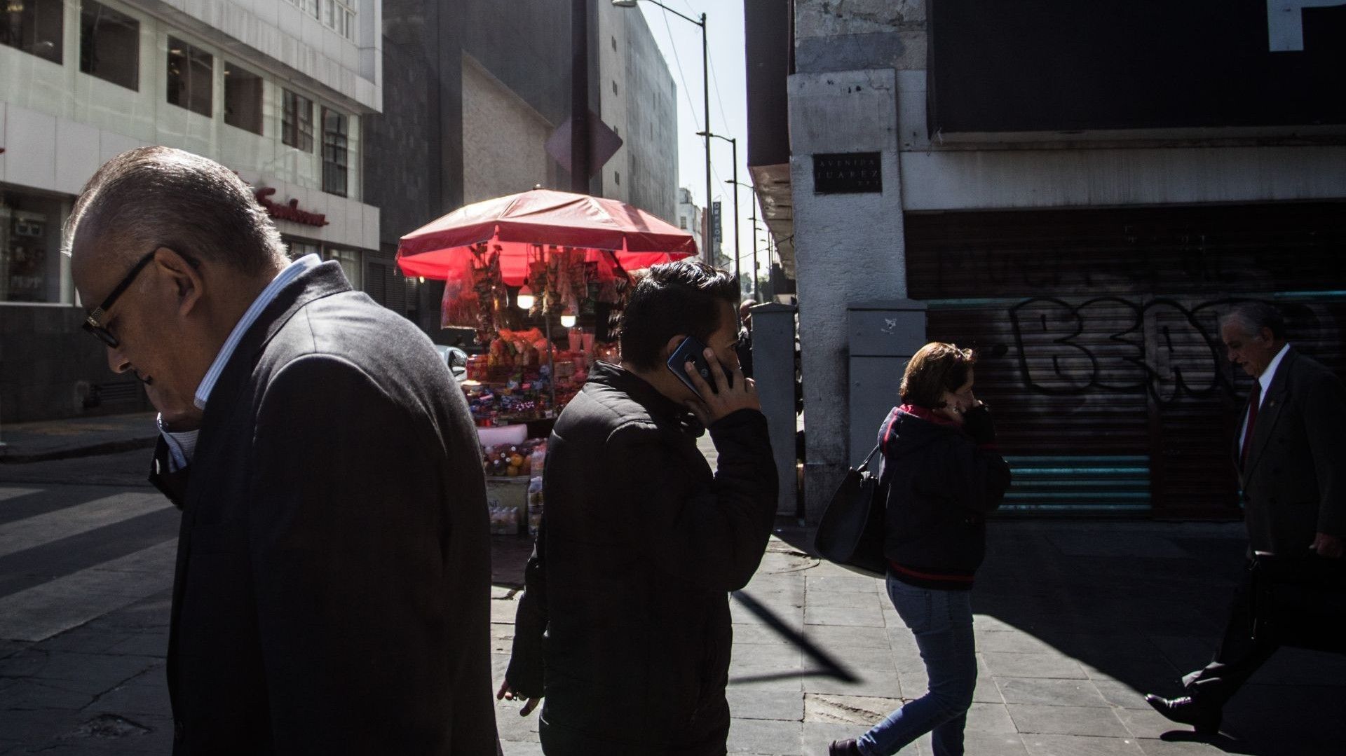 Personas caminan por la calle y contestan sus celulares.
