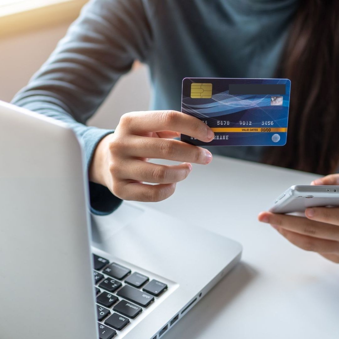 Una mujer tiene una tarjeta den la mano y está frente a la computadora.