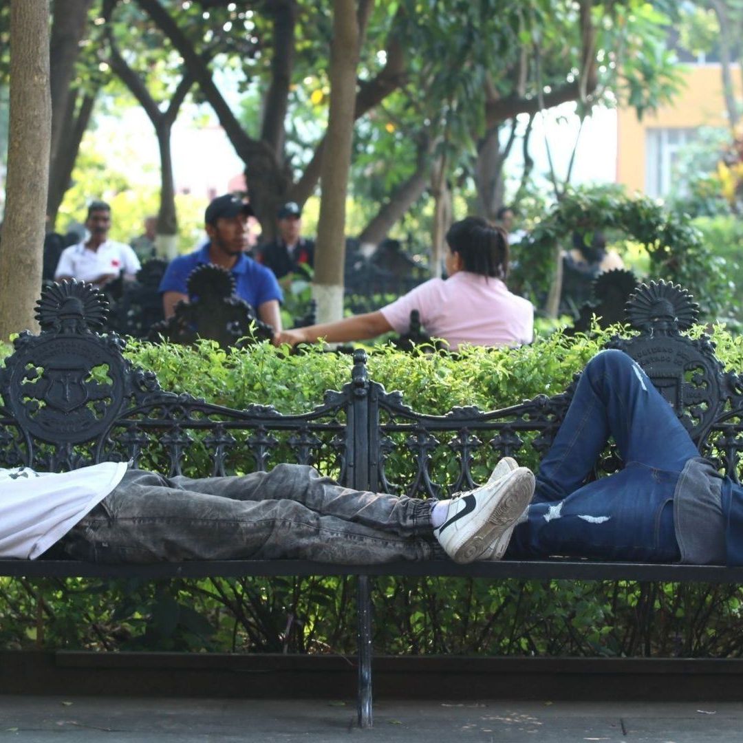 Dos hombres duermen en una banca.