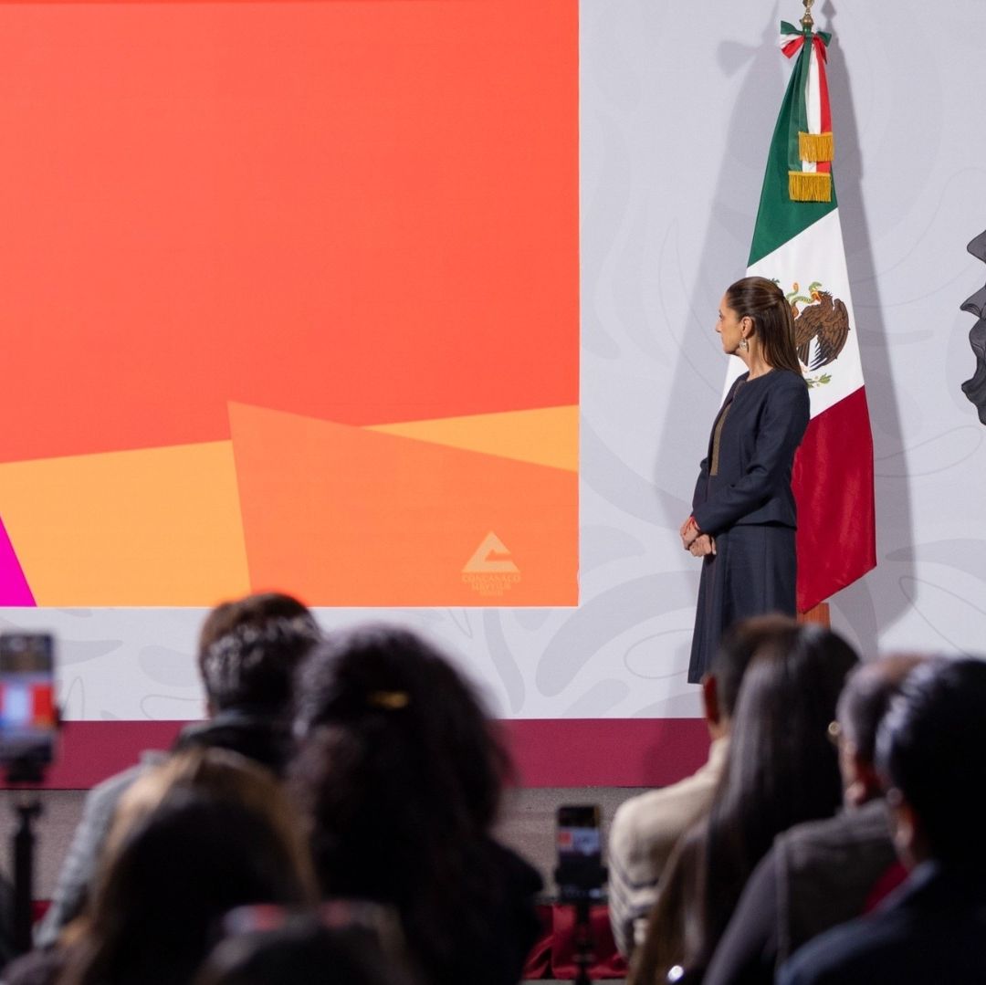 Una mujer viendo una pantalla, hay varias personas frente a ella.