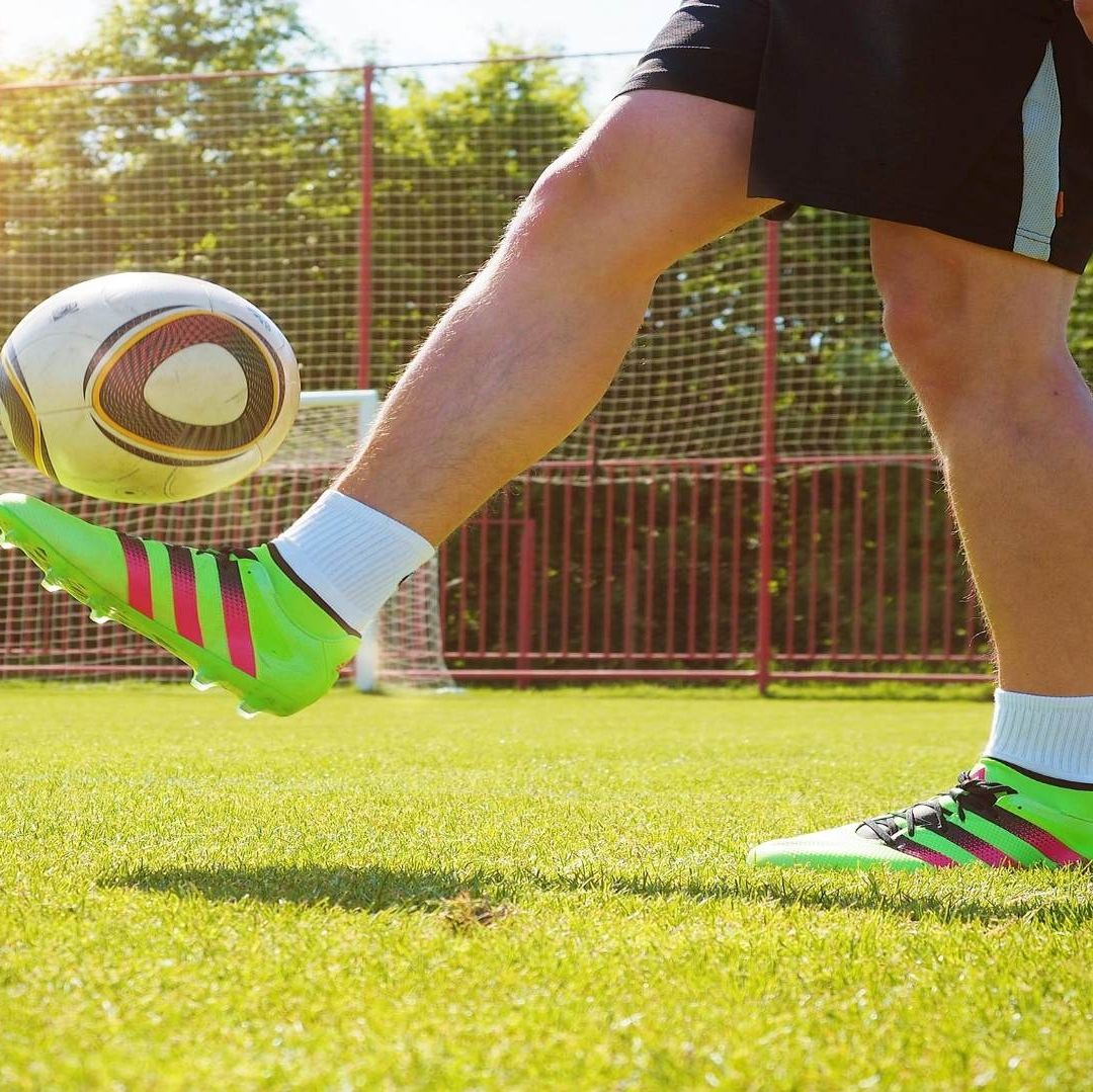 Un hombre está jugando con un balón, tiene unso tenis verdes y short negro.