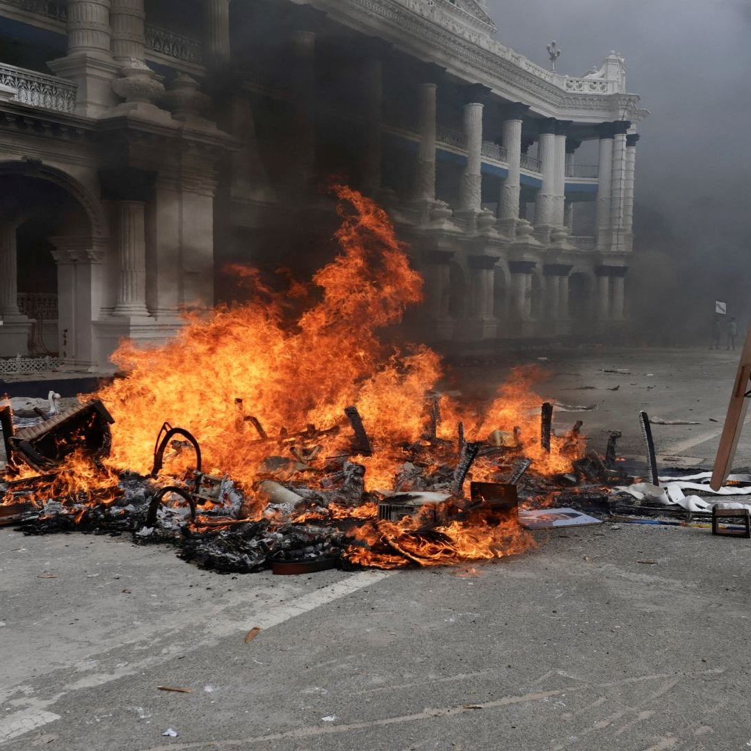 Un edificio blanco en medio de humo, un hombre lanza un objeto al fuego.
