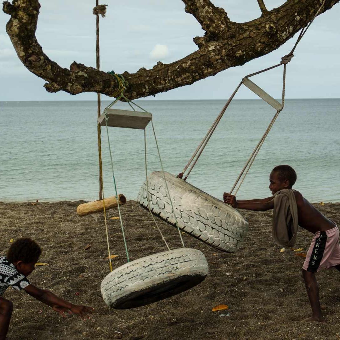 Niños juegan sobre un árbol arrancado de raíz en una playa de Mele, Vanuatu,