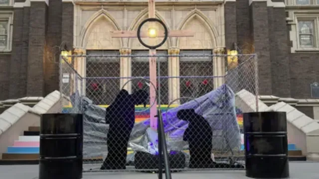 Frente a una iglesia, las siluetas de María y José están encerradas en un centro de detención para migrantes, separadas del niño Jesús.