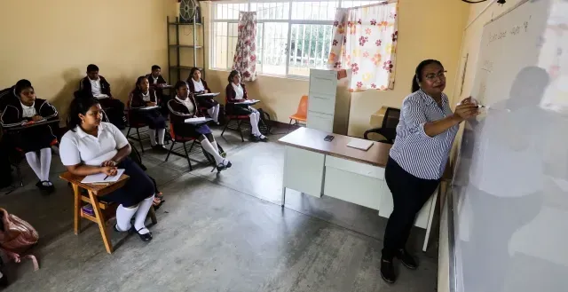 Maestra escribe en un pizarrón en el salón de clases