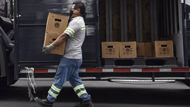 Un trabajador carga dos cartones de cerveza