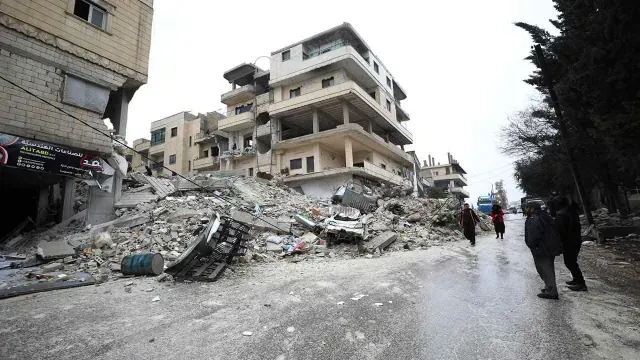 Personas caminan cerca de un edificio derrumbado tras sismo en Armanaz, Siria.
