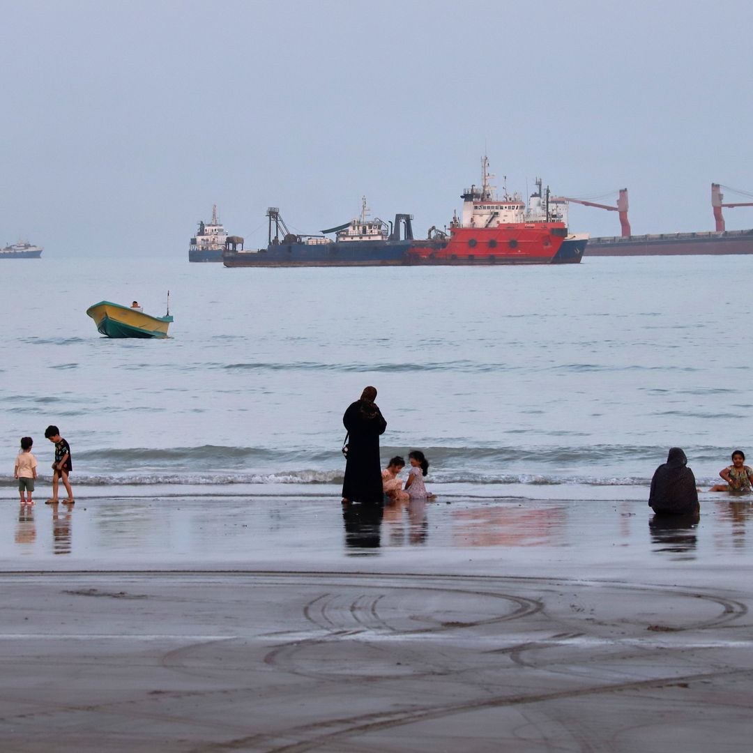 Personas en la playa, mientras al fondo se observan buques anclados en el Estrecho de Ormuz el 5 de agosto 2026.