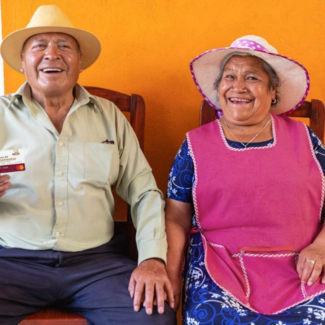 Una pareja de adultos mayores sostiene una tarjeta del Bienestar donde recibirán el pago de su Pensión Bienestar