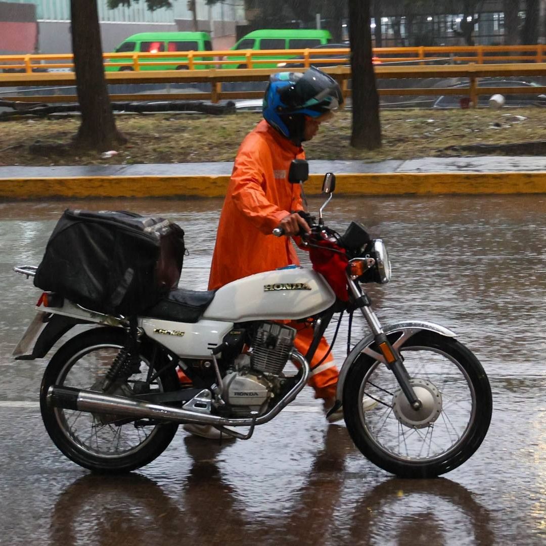 Un hombre camina junto a su moto y se protege de la lluvia en CDMX en agosto 2026. Foto: Cuartoscuro | Archivo