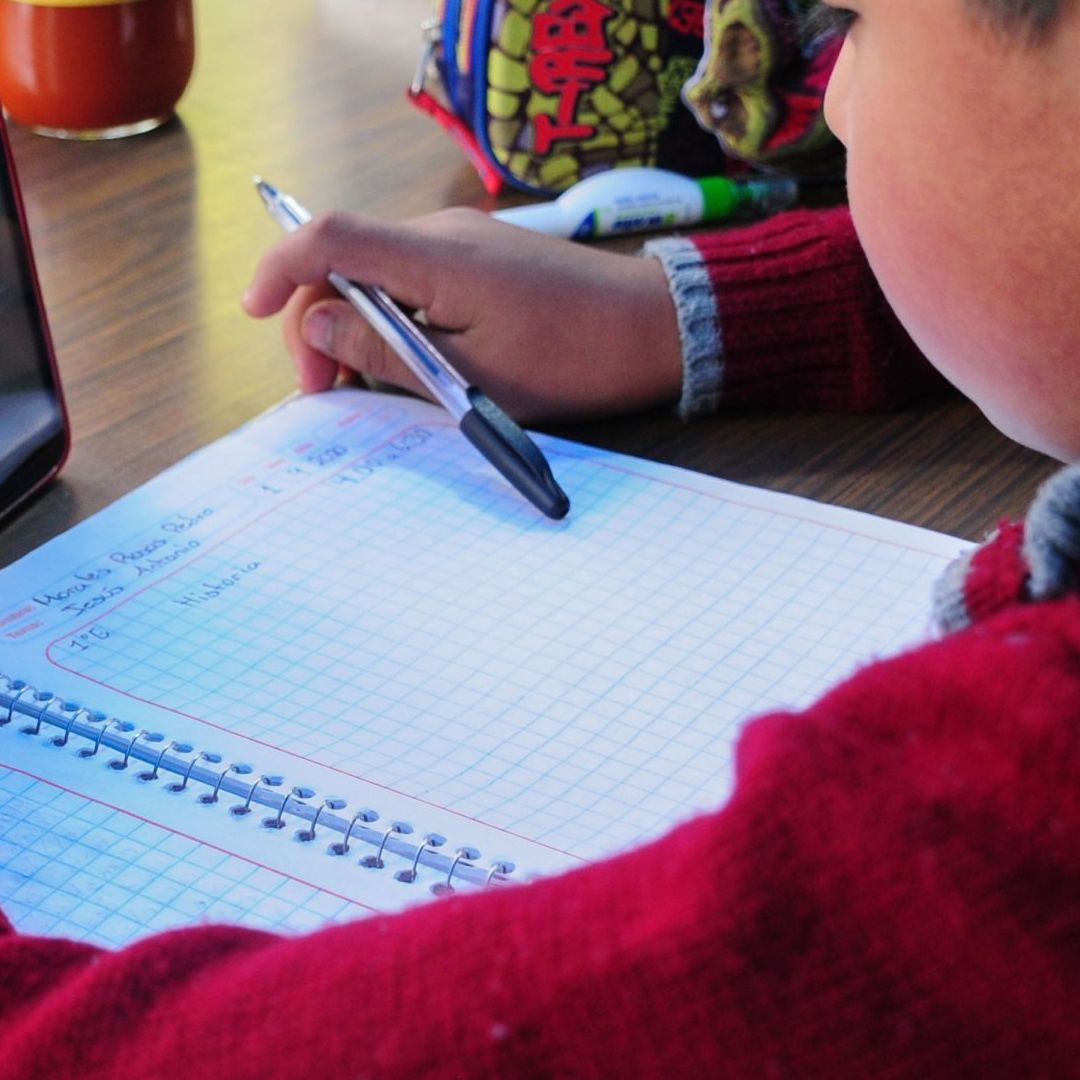 Un niño escribe en un cuaderno y ve un celular