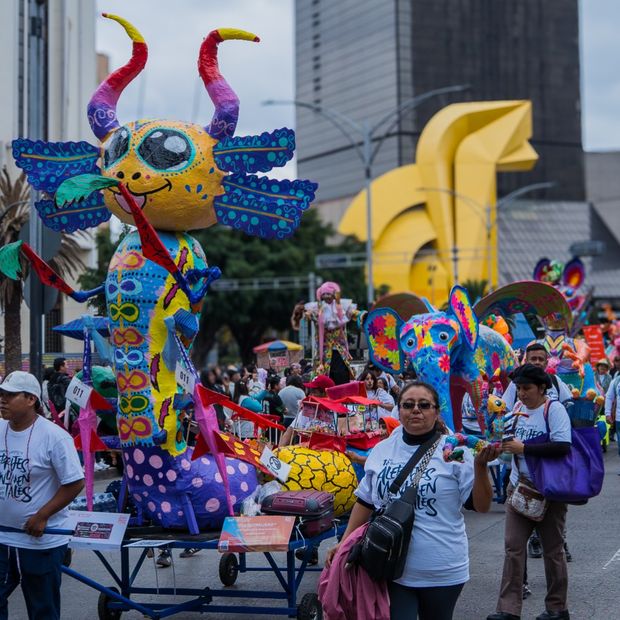 El alebrije "El Alebrijero" avanza sobre una carreta entre asistentes y zancudos durante el desfile. Foto: N+